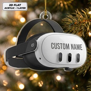 May include: A 2D flat acrylic ornament shaped like a virtual reality headset. The white front panel features the text CUSTOM NAME in dark gray, with three black sensor cutouts. A black strap wraps around the sides, and a gold string is attached.
