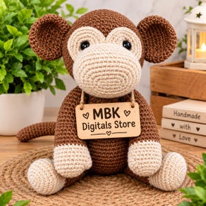Op de afbeelding: Een gehaakte apenknuffel in bruin en beige met grote ronde oren en zwarte veiligheidsoogjes. Een rechthoekig houten bordje hangt aan een touwtje van jute om de nek, met de zwarte tekst MBK Digitals Store en hartjesicoontjes.