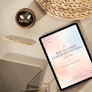 May include: A tablet displaying a digital journal titled "The 369 Guided Manifestation Journal" with a pink and blue gradient background. The text "99 Days of Manifesting" and "A journal from Bella Deluna Astrology" are also visible on the screen.