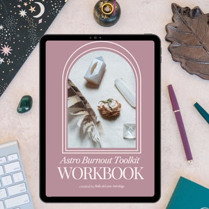 Puede incluir: Una tableta digital muestra el "Astro Burnout Toolkit WORKBOOK" con cristales, una pluma y flores secas. La tableta est&aacute; rodeada por un teclado, un bol&iacute;grafo y objetos decorativos sobre una superficie rosa claro.