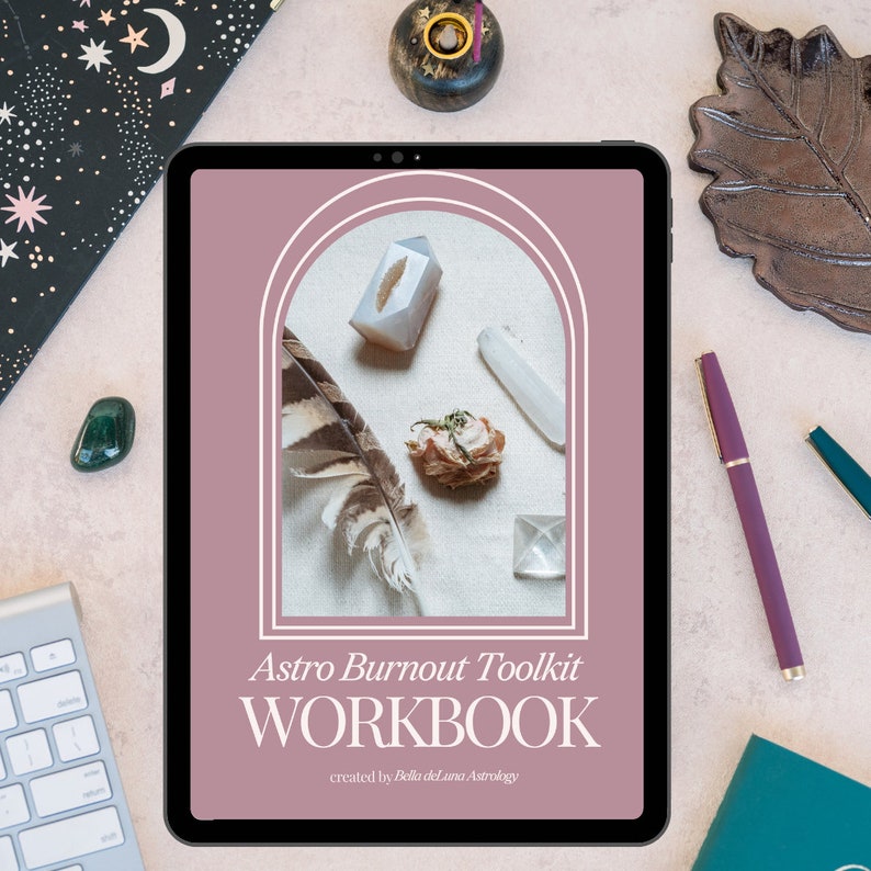 Puede incluir: Una tableta digital muestra el "Astro Burnout Toolkit WORKBOOK" con cristales, una pluma y flores secas. La tableta est&aacute; rodeada por un teclado, un bol&iacute;grafo y objetos decorativos sobre una superficie rosa claro.