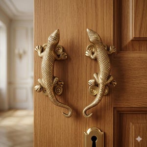 Puede incluir: Dos manijas de puerta de latón dorado con forma de lagarto, montadas en una puerta de madera. Las manijas de lagarto tienen patrones de escamas detallados. La puerta tiene una cerradura y un veteado de madera natural.