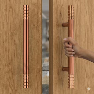 May include: A copper-colored door pull with a cylindrical design and tiered accents at each end. The door pull is mounted on a wooden door. One image shows the door pull being held by a hand.