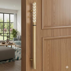 May include: A gold-colored door pull with a decorative woven design at the top. The long, cylindrical handle is mounted on a light brown wooden door. The door has a paneled design. The handle is a modern design element.