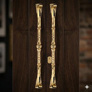 May include: Two ornate, gold-colored door handles are vertically centered against a dark brown wooden door. The handles have a detailed, elongated design with decorative elements and a keyhole between them. The background is blurred.