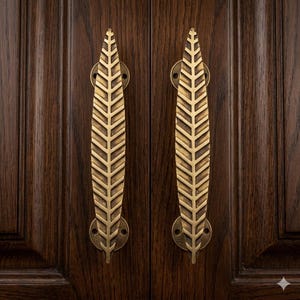 May include: Two brass-colored door handles with a leaf design are mounted on a dark brown wooden door. The handles are long and slender, with a detailed pattern resembling a feather. The door has vertical wood grain.