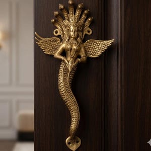May include: A detailed brass door handle featuring a mythical figure with a serpent tail, wings, and a multi-headed crown. The golden handle is mounted on a dark brown wooden door, showcasing intricate details and a unique design.