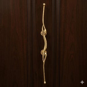 Puede incluir: Un tirador de puerta decorativo de color dorado con un diseño único y fluido. El tirador está montado en una puerta de madera marrón oscuro. El diseño presenta una forma curva y orgánica con detalles intrincados.