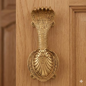 Pode incluir: Uma aldrava de porta de latão em forma de cobra. A aldrava está montada numa porta de madeira clara. A cabeça da cobra está levantada e o seu capuz está aberto. A aldrava tem detalhes intrincados e uma base oval decorativa.