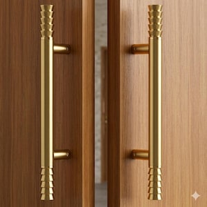 May include: Two gold-colored door pulls with a tiered design at the top and bottom. The pulls are mounted on a wooden door. The door has a natural wood grain finish.