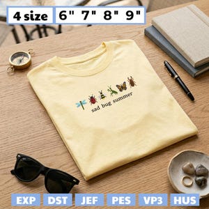 May include: A light yellow t-shirt with the text "sad bug summer" and embroidered insects. The shirt is displayed on a wooden surface with sunglasses, a compass, and a small dish. Sizes available: 6", 7", 8", and 9".