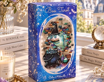 Könnte beinhalten: Eine rechteckige Boo Tarot Kartenschachtel mit blauem Farbverlauf und weißen Geister- und Sternenillustrationen. In der Mitte ist ein gezeichneter Geist mit Hexenhut zu sehen, der über einem schwarzen Kessel ein Buch liest, mit dem Text Boo Tarot.