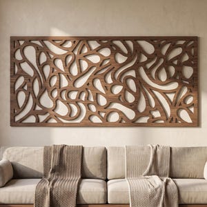 May include: A rectangular wall art piece made of dark brown wood featuring an intricate, laser-cut pattern of interconnected, flowing organic shapes and curves. The wooden panel is mounted horizontally on a plain, light-coloured interior wall.