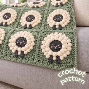 Può includere: Una coperta all'uncinetto con un motivo quadrato ripetuto e bordi verde salvia. Ogni quadrato presenta un motivo centrale a pecora con viso grigio scuro, guance rosa e un corpo in lana testurizzato realizzato a punto nocciolina crema.