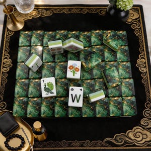 May include: A set of Mahjong tiles featuring a dark green and gold marbled pattern on the back. Several tiles are face up, displaying white surfaces with colorful illustrations of a peacock, flowers, and the letter W with the Chinese character for West.