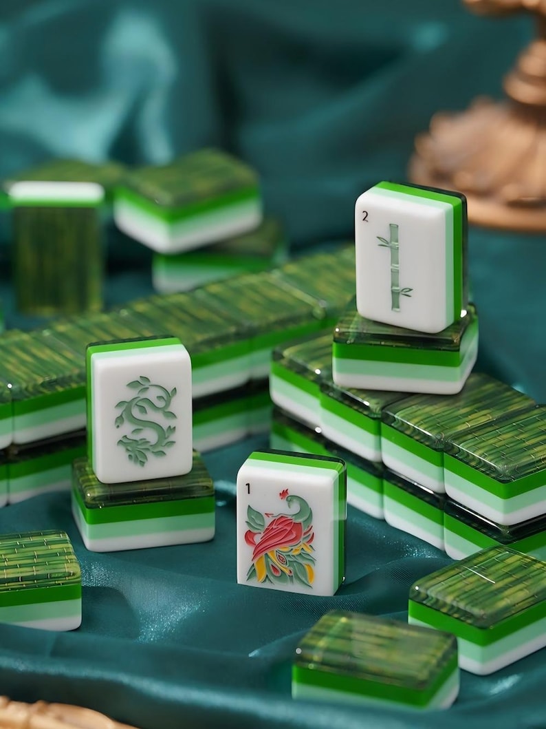 May include: A collection of rectangular mahjong tiles featuring a layered design with a white top section and a translucent green base. The tiles display engraved symbols including a green bamboo stalk, a green dragon, and a colorful bird illustration.