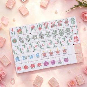May include: A set of white Mahjong tiles featuring colorful floral, bamboo, and character designs, including tiles marked with the letters N, E, W, S and the word JOKER. The tiles are arranged in a grid, surrounded by scattered pink flower petals.