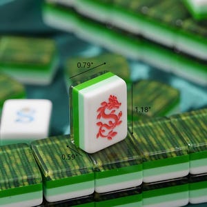 May include: A set of Mahjong tiles featuring a white face with a red dragon engraving. The tiles have a layered design with a green and white base and a translucent green top. Dimensions are clearly marked as 0.79 inches wide, 1.18 inches tall, and 0.59 inches deep.