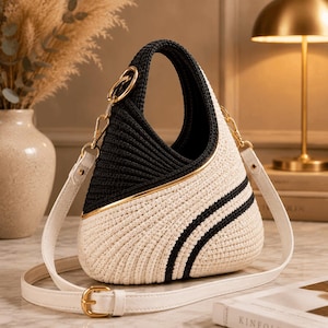 Può includere: Una borsa strutturata dal design bicolore con una sezione superiore nera e una inferiore color crema, entrambe realizzate in materiale cordato testurizzato. La borsa presenta finiture in metallo dorato, un manico superiore e una tracolla bianca rimovibile.