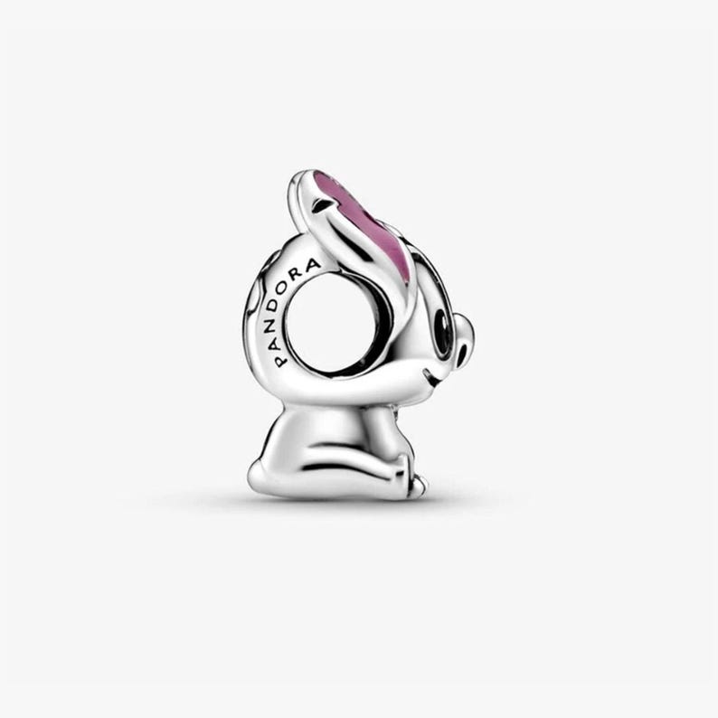 May include: A silver charm bead shaped like a cartoon character with large ears, featuring pink enamel detailing on the inner ears and the word PANDORA engraved along the side of the circular opening. The charm has a smooth, polished metallic finish.
