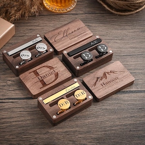 May include: Wooden boxes with personalized cufflinks and tie clips. The boxes are engraved with names and initials. The cufflinks are silver and gold, with initials. A watch and a gift box are also visible.