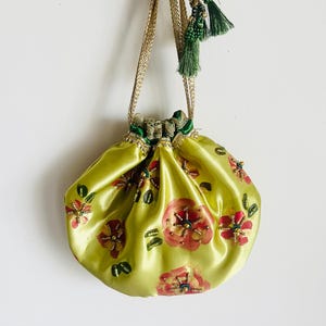 May include: A lime green satin drawstring pouch featuring a floral pattern with pink and red painted flowers, accented by small beads. The bag has a gold metallic braided handle and a green fabric drawstring closure with green beaded tassels.
