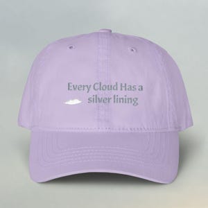 Può includere: Un cappellino da baseball color viola chiaro con il testo ricamato Every Cloud Has a silver lining, accompagnato da una piccola grafica bianca a forma di nuvola posizionata a sinistra della parola silver sul pannello frontale.