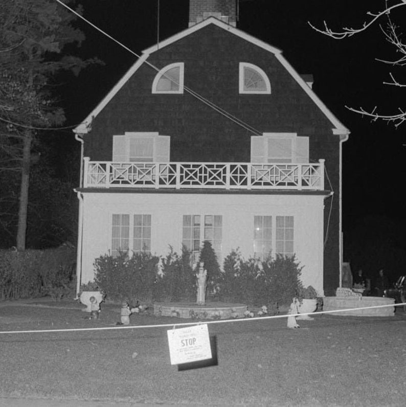 May include: Black and white image of a two-story house at night. The house has a dark roof, white siding, and a balcony with decorative railings. A sign in front reads "STOP".