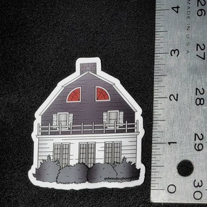 May include: A sticker featuring a two-story house with a dark gray roof and red arched windows. The house has white siding, a small balcony, and a row of bushes at the base. The text "@dwindlinghourglass" is at the bottom.