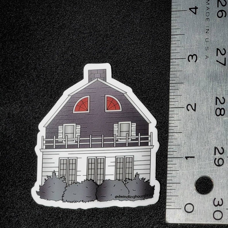 May include: A sticker featuring a two-story house with a dark gray roof and red arched windows. The house has white siding, a small balcony, and a row of bushes at the base. The text "@dwindlinghourglass" is at the bottom.