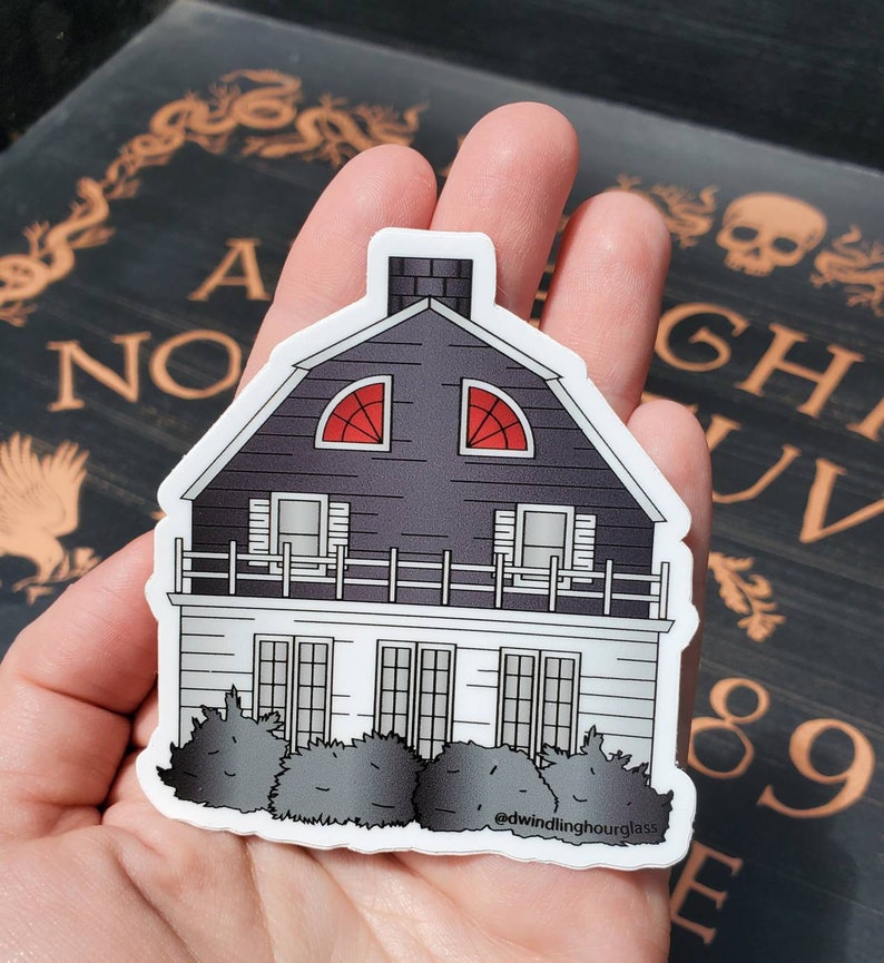 May include: A sticker featuring a stylized illustration of a house with a dark gray roof and white siding. The house has two red arched windows and a chimney. The sticker includes the text "@dwindlinghourglass".