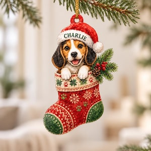 May include: A Christmas tree ornament featuring a beagle puppy wearing a red Santa hat with the name CHARLIE printed on the white trim. The puppy is inside a red and green stocking decorated with snowflake and paw print patterns.