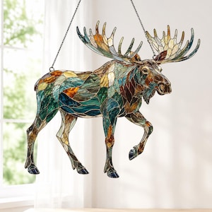 Op de afbeelding: Een hangend elandornament van glas-in-lood, bestaande uit een mozaïek van veelkleurige glasstukjes in tinten blauwgroen, amber, bruin en crème. De eland is afgebeeld in een lopende houding met een groot gewei, opgehangen aan een dunne ketting.