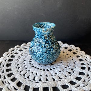Peut inclure: Un petit vase en céramique avec un corps bulbeux et un bord évasé, présentant un émail cristallin texturé dans des tons de bleu profond, bleu clair et blanc, créant un motif organique et bouillonnant sur toute la surface extérieure.