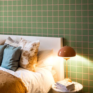 Peut inclure: Une chambre avec une tête de lit blanche, une couette blanche et un jeté de lit marron texturé. Les oreillers sont bleu uni, blancs avec des motifs de palmiers marron, et noirs et blancs. Une lampe dôme pêche est posée sur une table ronde.