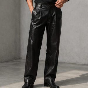 Pode incluir: Uma camisa preta de manga comprida com colarinho e punhos, combinada com calças de couro pretas de cintura alta, com pregas na frente e corte de perna reta, usadas com sapatos de couro pretos.
