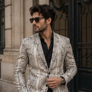 May include: A blazer featuring a grey and white snakeskin pattern, worn over a solid black button-down shirt. The blazer has a notched lapel, two front buttons, and two flap pockets. The ensemble is paired with dark-tinted sunglasses and a watch.