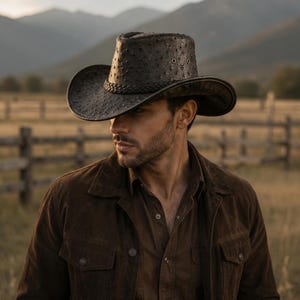 May include: A dark brown cowboy hat with a textured, dotted surface pattern, a braided band around the base of the crown, and metal eyelets on the sides. The hat features a wide, curved brim and a structured crown, crafted in a deep, earthy tone.