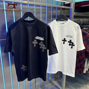以下が含まれることがあります： 半袖でクルーネックの黒いTシャツと白いTシャツ。胸元には「Off-White NEW YORK」の文字がプリントされています。それぞれのシャツの前面には、黒い十字架型のパッチが複数あしらわれています。