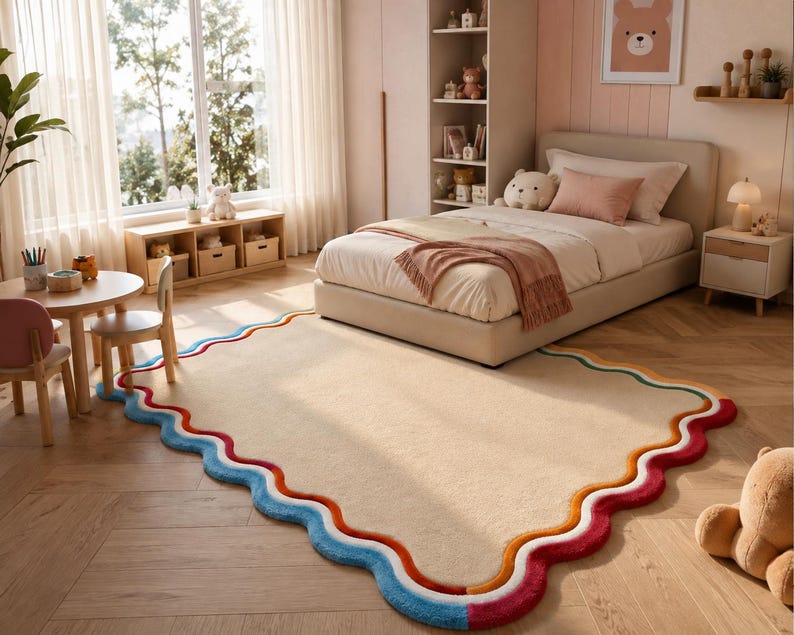 May include: A rectangular area rug with a solid beige center and a scalloped, wavy border featuring layered bands of orange, white, and blue colors. The rug has a soft, plush texture and is positioned on a light-colored wooden floor.