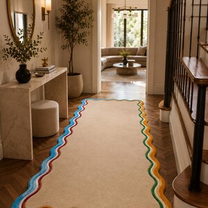May include: A rectangular runner rug with a solid beige center and a wavy, scalloped border featuring concentric bands of blue, white, green, yellow, and red. The rug is positioned on a dark wood floor in a hallway, extending from the foreground.