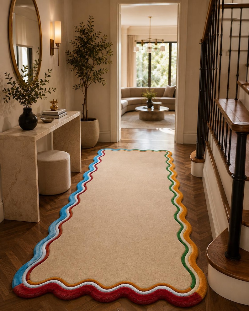 May include: A rectangular runner rug with a solid beige center and a wavy, scalloped border featuring concentric bands of blue, white, green, yellow, and red. The rug is positioned on a dark wood floor in a hallway, extending from the foreground.