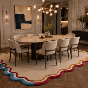 May include: A large, irregularly shaped area rug featuring a beige center and a wavy, multi-colored border in shades of blue, yellow, orange, and magenta. The rug is positioned beneath an oval dining table with six upholstered chairs.