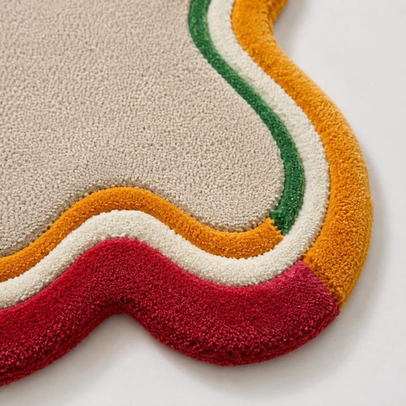 May include: A tufted rug with an irregular, organic shape featuring a large beige center surrounded by concentric, wavy borders in green, cream, mustard yellow, and deep red. The surface has a dense, textured pile with a soft, looped appearance.