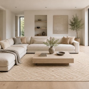 Puede incluir: Salón moderno con un gran sofá esquinero blanco roto y varios cojines. Una mesa de centro de madera clara se encuentra sobre una alfombra estampada. Jarrones decorativos y un pequeño árbol completan la estética minimalista.