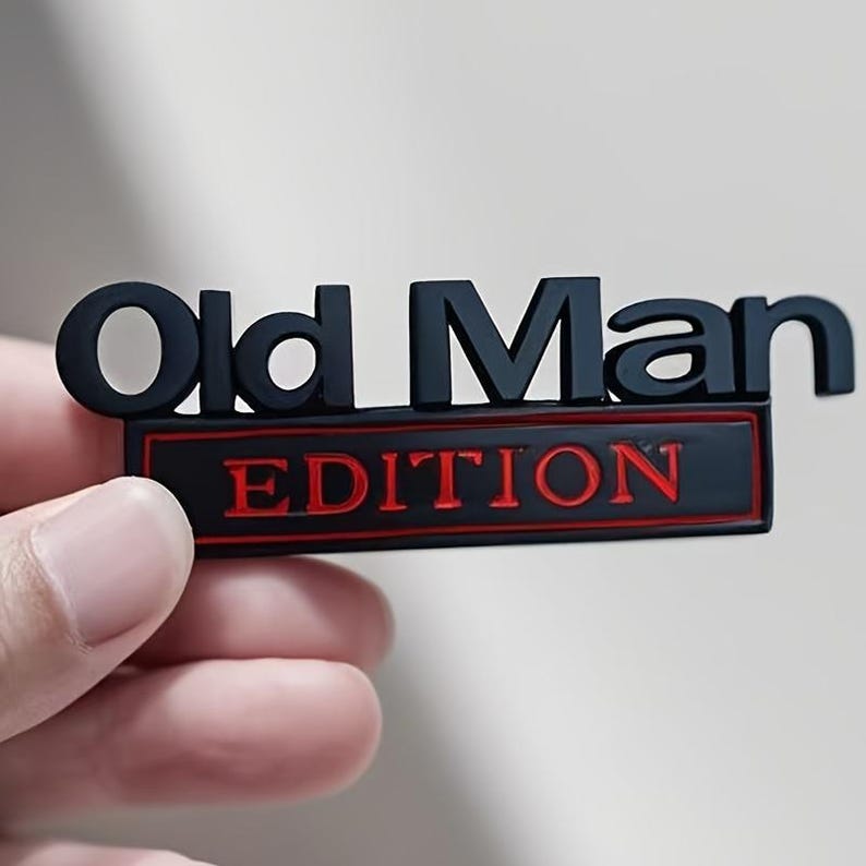 Pu&ograve; includere: Un emblema nero e rosso con le parole "Old Man EDITION". Il testo &egrave; in grassetto, senza grazie. La parola "Old Man" &egrave; in nero e "EDITION" &egrave; in rosso. L'emblema &egrave; tenuto da una mano.