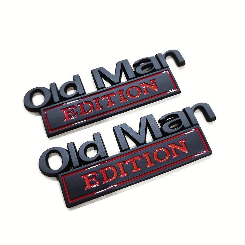 Pu&ograve; includere: Due emblemi neri "Old Man Edition" con scritte rosse. Il testo &egrave; in rilievo e ha un effetto 3D. Gli emblemi sono rettangolari con angoli arrotondati, su sfondo bianco.