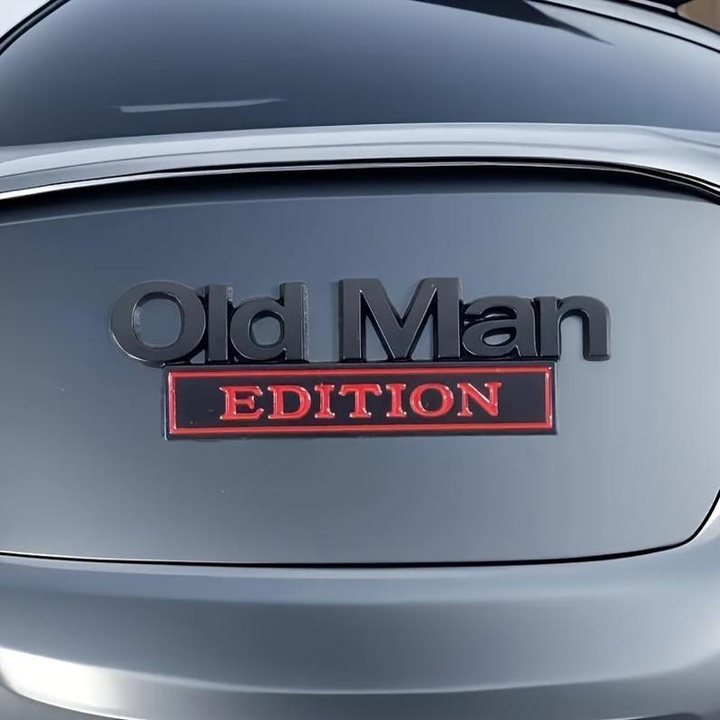 Pu&ograve; includere: Un'auto grigio scuro con un emblema nero che recita "Old Man EDITION" in grassetto. La parola "EDITION" &egrave; in un rettangolo rosso, aggiungendo un colore contrastante al design generale.