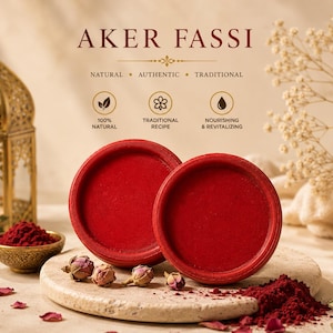 Può includere: L'immagine presenta due contenitori rotondi rossi, con il testo "AKER FASSI" in alto. I contenitori sono posizionati su una superficie di pietra, circondati da boccioli di rosa e polvere rossa. Sono visibili anche una lanterna dorata decorativa e una piccola ciotola di polvere rossa.