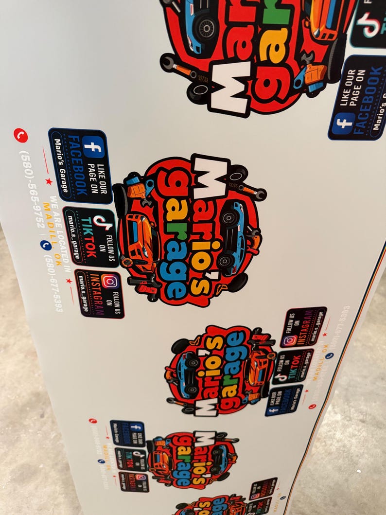 May include: A white promotional sign featuring multiple repeating logos for Mario's Garage. Each logo displays a red circular background with a blue car, tools, and the text Mario's Garage. Social media icons for Facebook, TikTok, and Instagram are included.